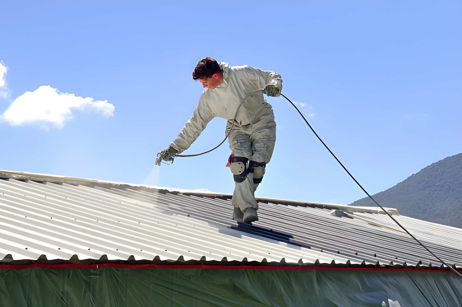 A trademan uses an airless spray to paint the roof of a building