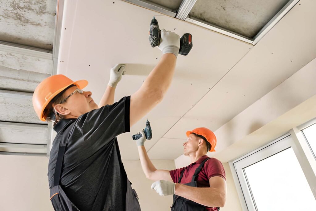 Workers are using screws and a screwdriver to attach plasterboard to the ceiling.