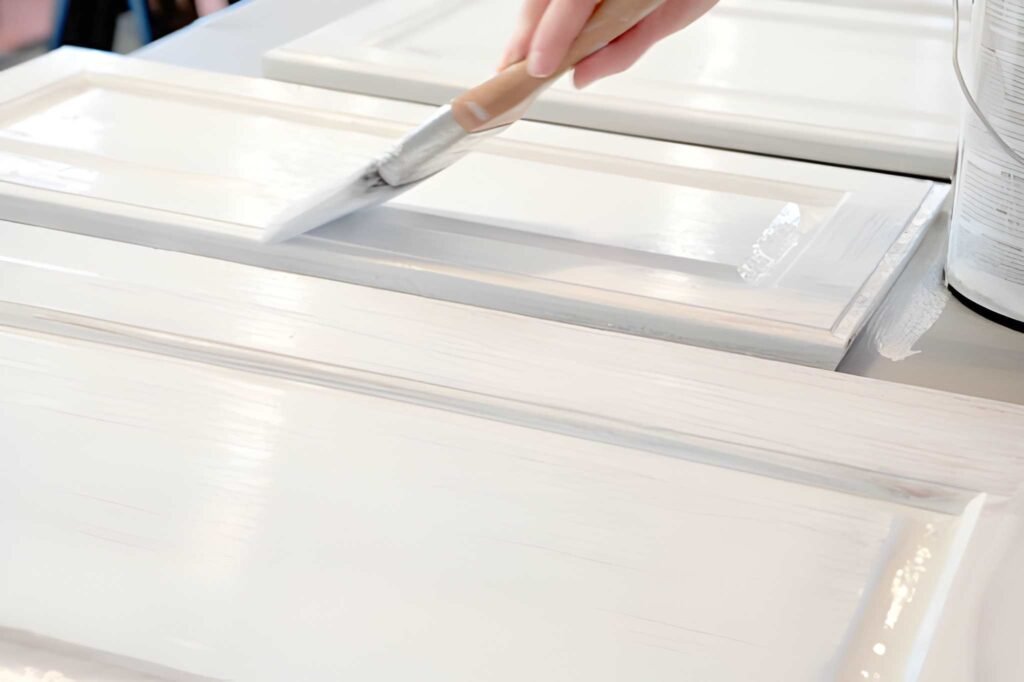 Hand applying white paint to cabinet door.