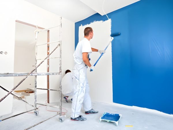 House painters beginning to paint a large blue wall. Professional house painters in bright room.